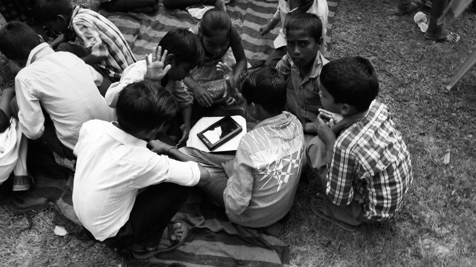 Children gathered around a tablet on the grass, watching a film they made